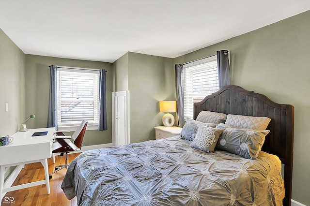 bedroom with multiple windows, wood finished floors, and baseboards