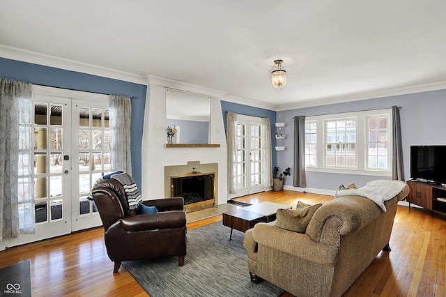 living area with a brick fireplace, wood-type flooring, ornamental molding, and french doors