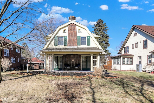 back of house featuring covered porch, brick siding, a chimney, and a gambrel roof