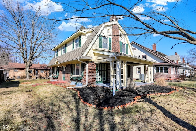 view of front of house featuring brick siding, a shingled roof, a gambrel roof, a chimney, and a front yard