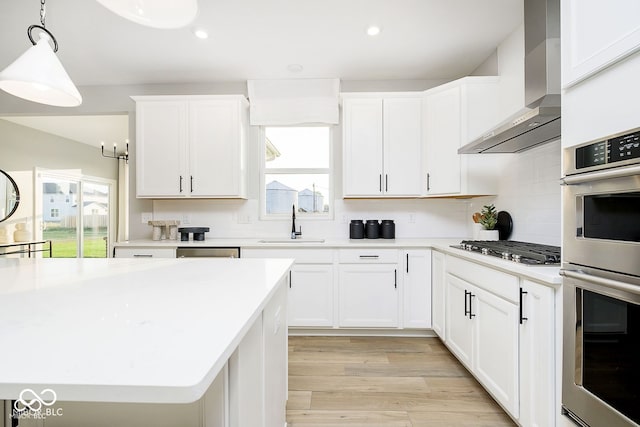 kitchen featuring a healthy amount of sunlight, stainless steel appliances, wall chimney range hood, and a sink