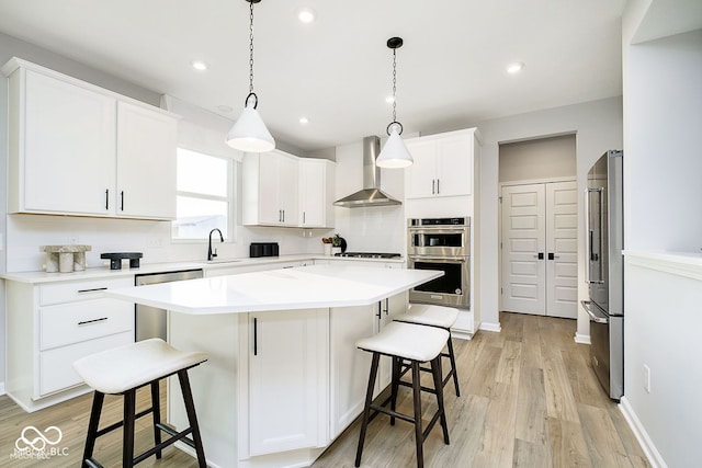 kitchen with a kitchen island, wall chimney range hood, a kitchen breakfast bar, white cabinets, and stainless steel appliances