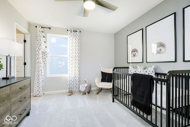 carpeted bedroom featuring a crib, a ceiling fan, and baseboards