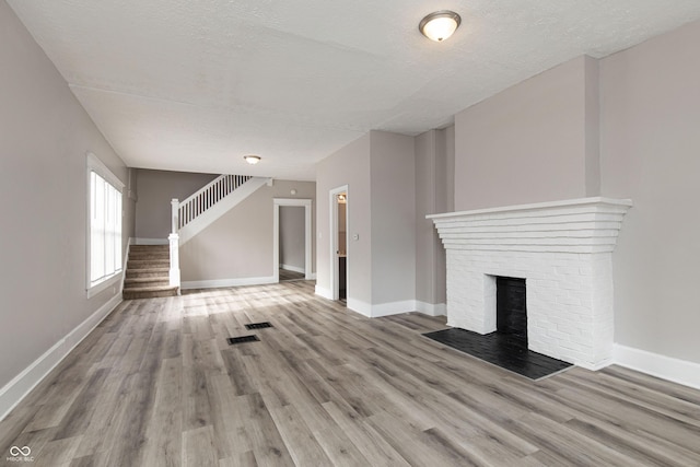 unfurnished living room featuring a brick fireplace, light hardwood / wood-style flooring, and a textured ceiling