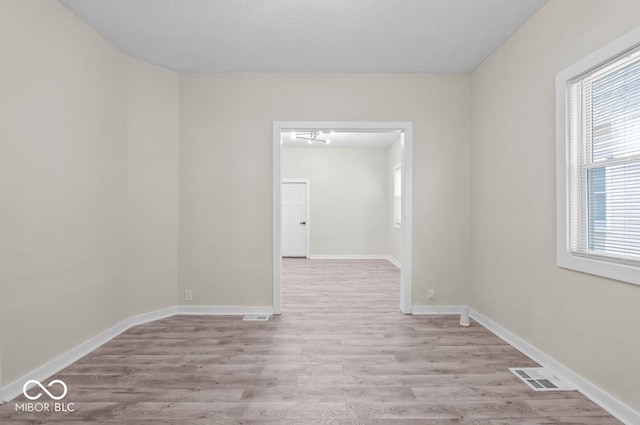 spare room with plenty of natural light, a textured ceiling, and light wood-type flooring