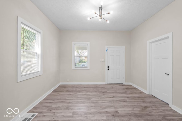 empty room with a textured ceiling, a chandelier, and light hardwood / wood-style flooring