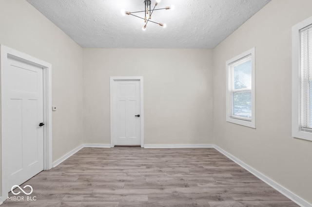 empty room featuring a chandelier, a textured ceiling, and light wood-type flooring