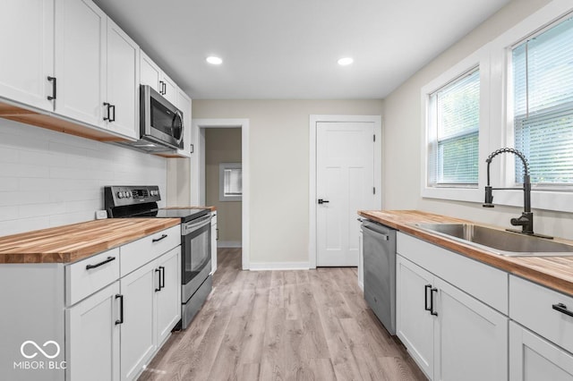 kitchen with white cabinetry, wood counters, stainless steel appliances, and sink