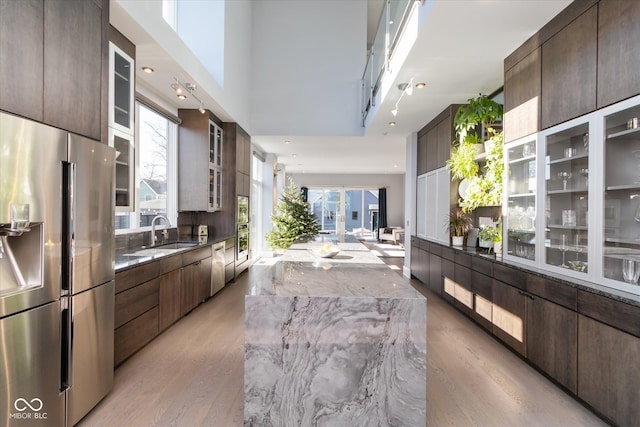 kitchen with sink, dark brown cabinetry, light stone counters, stainless steel fridge with ice dispenser, and light wood-type flooring