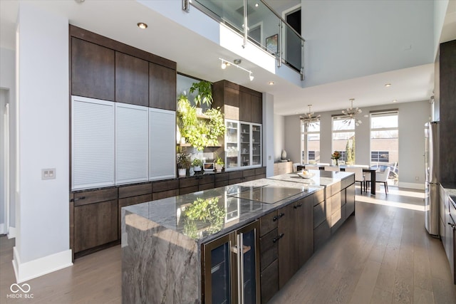 kitchen with hardwood / wood-style flooring, dark stone countertops, a spacious island, a high ceiling, and wine cooler