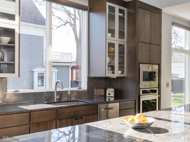 kitchen with backsplash, appliances with stainless steel finishes, sink, and dark stone countertops