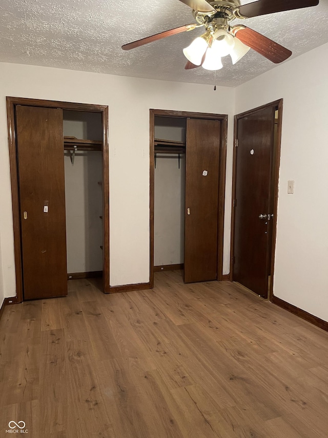 unfurnished bedroom with ceiling fan, two closets, a textured ceiling, and light hardwood / wood-style floors