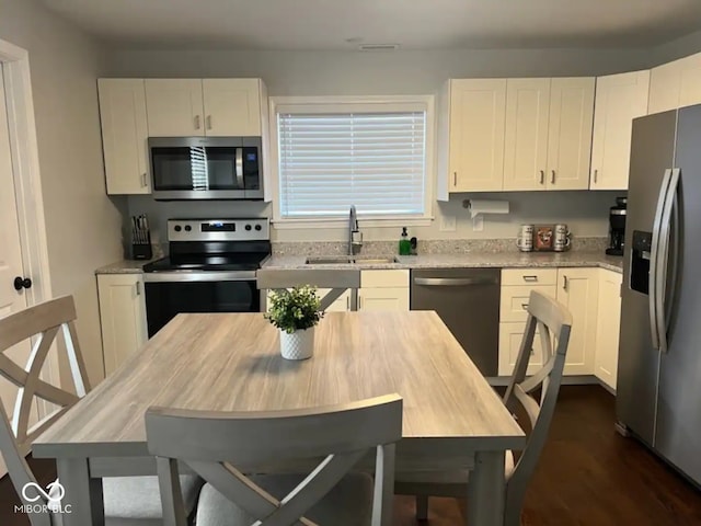 kitchen with a sink, stainless steel appliances, light stone countertops, and white cabinets