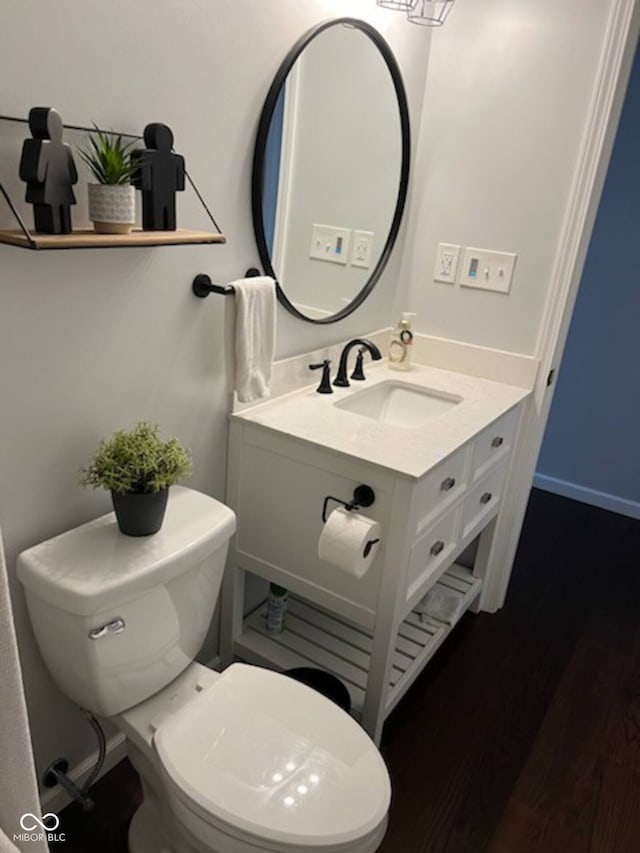 half bath with toilet, vanity, baseboards, and wood finished floors