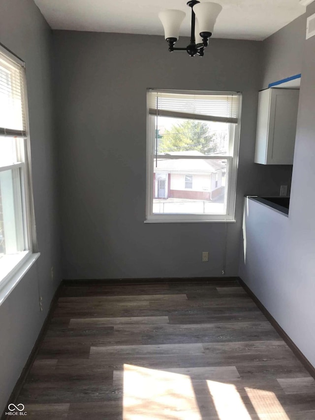 unfurnished dining area with a notable chandelier, dark wood-type flooring, and plenty of natural light