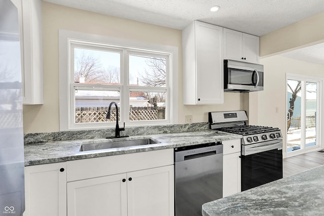 kitchen featuring appliances with stainless steel finishes, sink, white cabinets, light stone countertops, and a textured ceiling