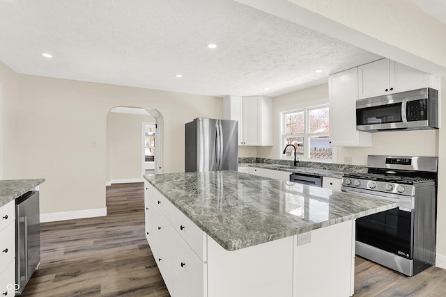 kitchen featuring appliances with stainless steel finishes, wood-type flooring, white cabinets, a center island, and a textured ceiling