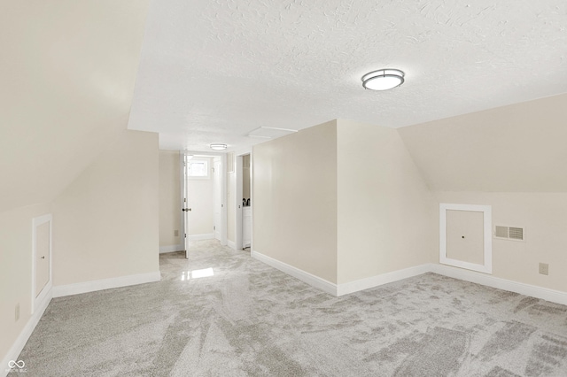 additional living space featuring vaulted ceiling, light colored carpet, and a textured ceiling