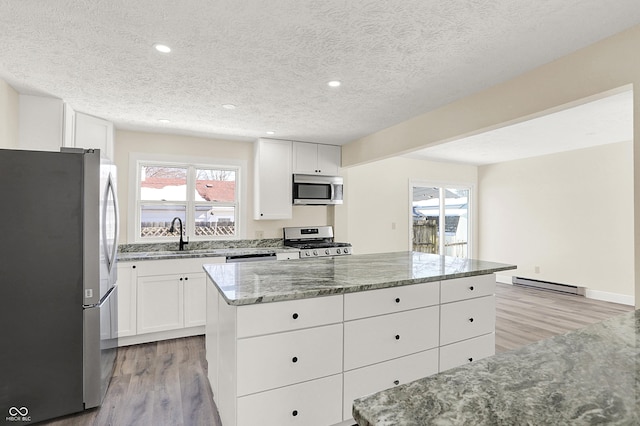 kitchen featuring appliances with stainless steel finishes, white cabinetry, a center island, baseboard heating, and a textured ceiling