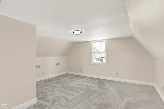 bonus room with lofted ceiling, light colored carpet, and a textured ceiling