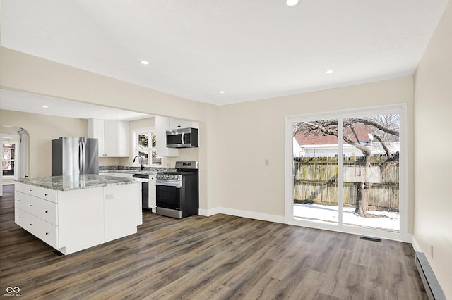 kitchen with dark wood-type flooring, baseboard heating, stainless steel appliances, white cabinets, and a kitchen island