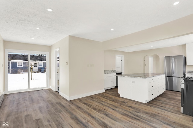 kitchen with dark wood-type flooring, stainless steel refrigerator, white cabinetry, a center island, and light stone counters