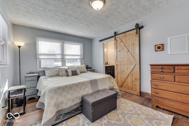 bedroom with a barn door, a textured ceiling, and light wood-type flooring