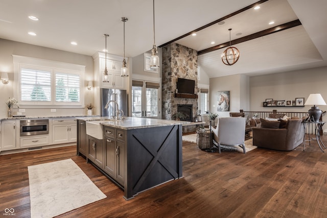 kitchen featuring light stone counters, pendant lighting, an island with sink, and white cabinets