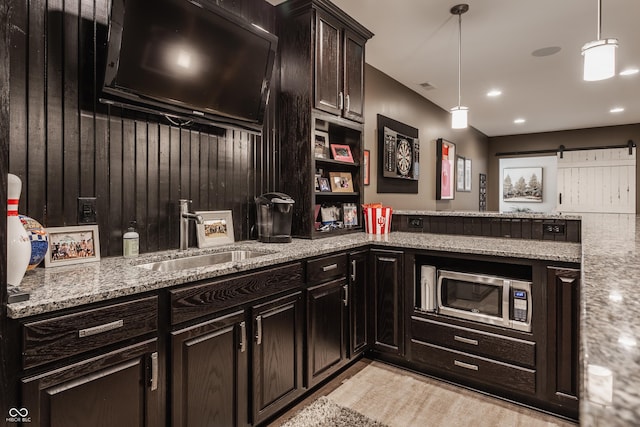 kitchen with sink, dark brown cabinetry, light stone countertops, decorative light fixtures, and a barn door