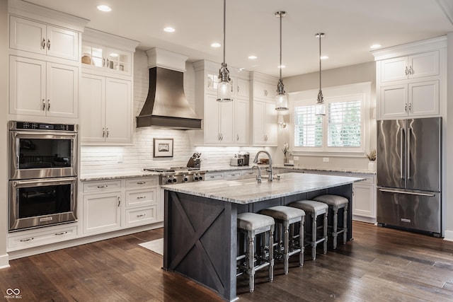 kitchen featuring custom exhaust hood, stainless steel appliances, white cabinets, and a center island with sink