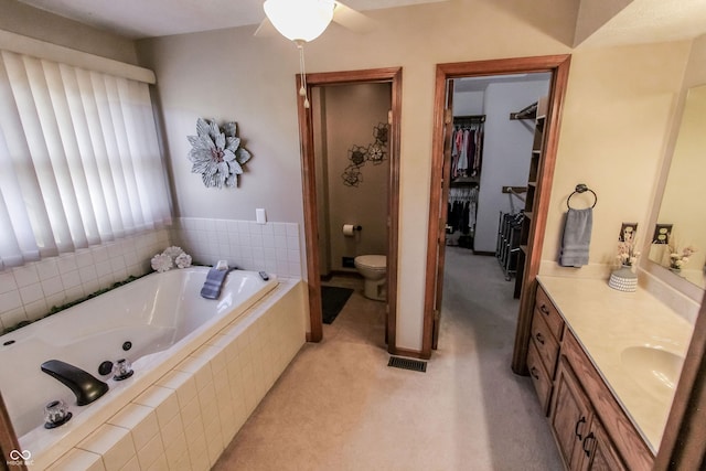 bathroom with a relaxing tiled tub, vanity, and toilet