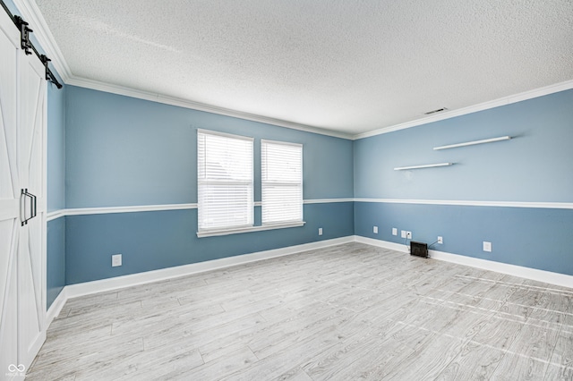 spare room featuring ornamental molding, a barn door, light hardwood / wood-style flooring, and a textured ceiling