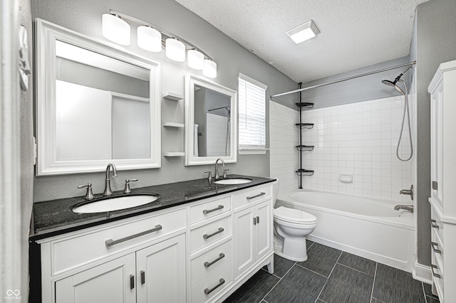 full bathroom with tiled shower / bath, vanity, toilet, and a textured ceiling