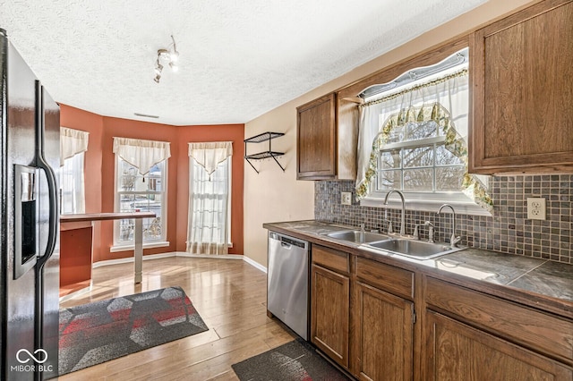 kitchen with sink, black refrigerator with ice dispenser, stainless steel dishwasher, light hardwood / wood-style floors, and backsplash