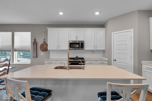 kitchen featuring an island with sink, a kitchen bar, white cabinets, and backsplash