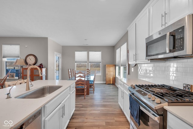 kitchen featuring sink, white cabinetry, light wood-type flooring, stainless steel appliances, and backsplash