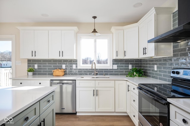 kitchen with decorative light fixtures, white cabinetry, sink, stainless steel appliances, and wall chimney range hood