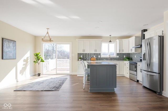 kitchen featuring a kitchen island, white cabinets, hanging light fixtures, stainless steel appliances, and wall chimney exhaust hood