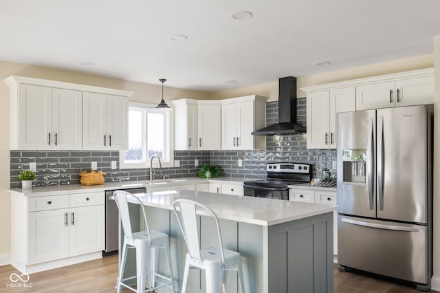 kitchen with a kitchen island, decorative light fixtures, white cabinets, stainless steel appliances, and wall chimney range hood