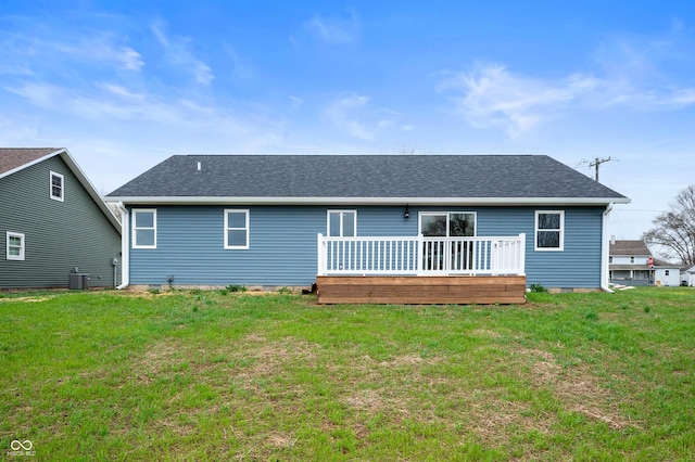 rear view of house with cooling unit, a shingled roof, a wooden deck, and a lawn