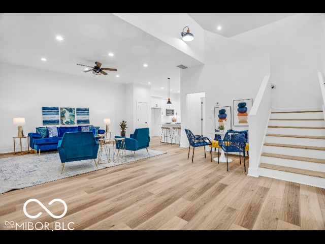 living room with ceiling fan, a high ceiling, and light wood-type flooring