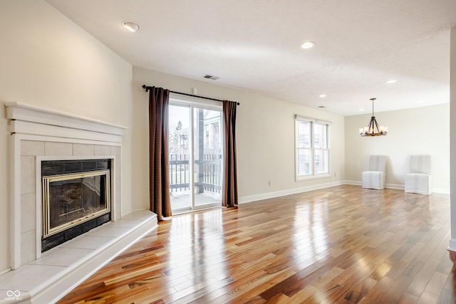 unfurnished living room featuring a tiled fireplace, a notable chandelier, and light hardwood / wood-style floors