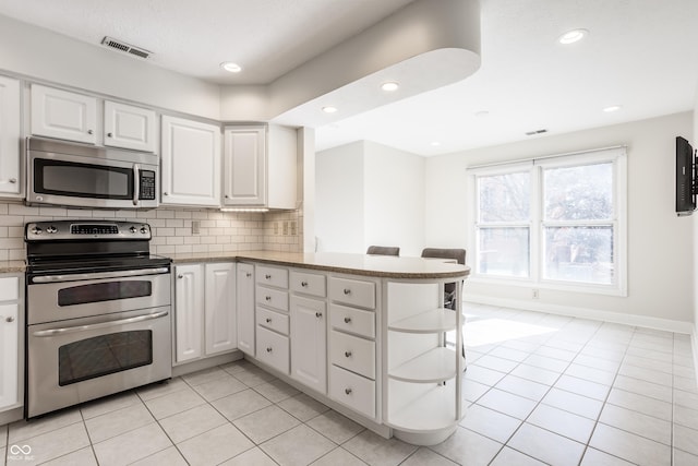 kitchen featuring white cabinets, decorative backsplash, light tile patterned floors, kitchen peninsula, and stainless steel appliances