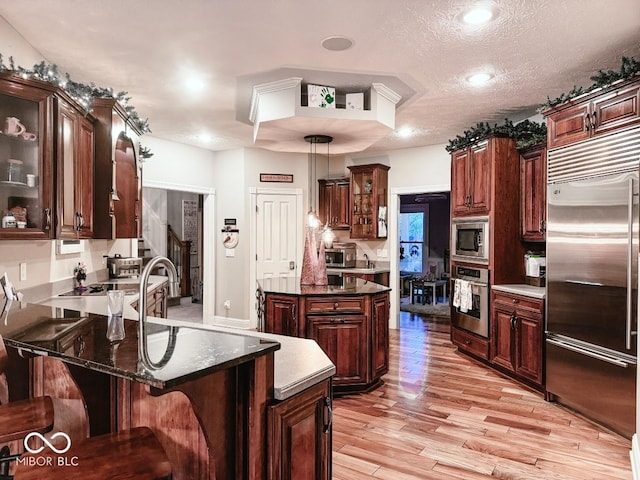 kitchen with built in appliances, a center island, hanging light fixtures, a textured ceiling, and light hardwood / wood-style floors