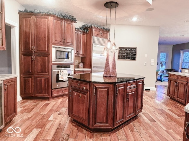 kitchen with hanging light fixtures, dark stone countertops, built in appliances, and light hardwood / wood-style flooring