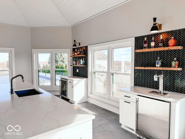 kitchen featuring lofted ceiling, sink, white cabinets, beverage cooler, and light stone countertops