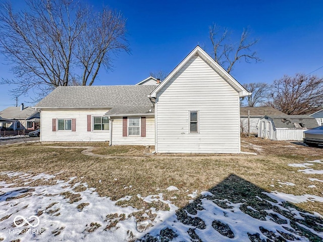 snow covered rear of property with a storage unit and a lawn