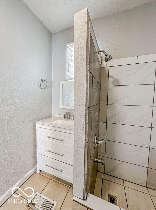 bathroom featuring tiled shower, tile patterned floors, a textured ceiling, and vanity