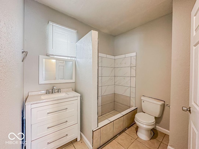 bathroom with tile patterned flooring, vanity, toilet, and tiled shower