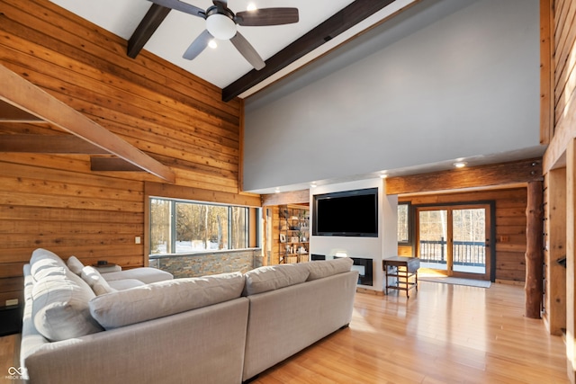 living room featuring high vaulted ceiling, light wood-type flooring, wooden walls, ceiling fan, and beam ceiling